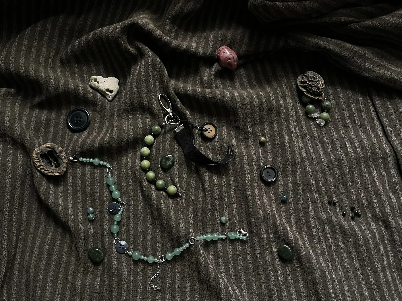 Jay Nest collection jewelry arranged on dark striped cloth